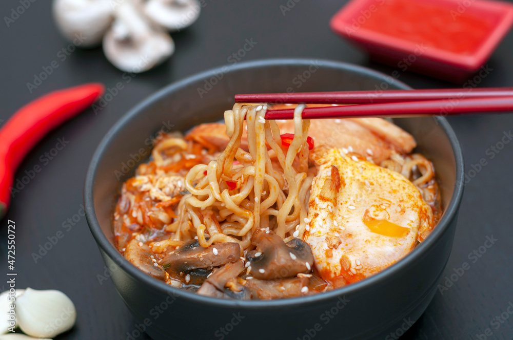 chopsticks hold Ramen - a national, popular dish of traditional Korean cuisine. Asian soup with noodles, chicken breast, egg, mushrooms, broth, hot sauce and spices. chopsticks hold Ramen - a national, popular dish of traditional Korean cuisine. Asian soup with noodles, chicken breast, egg, mushrooms, broth, hot sauce and spices.