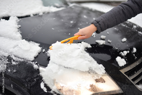  A hand sweeps snow from the hood of the car.