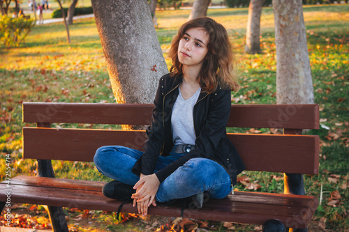 Cheerful teenager girl sitting on the bench at autumn park