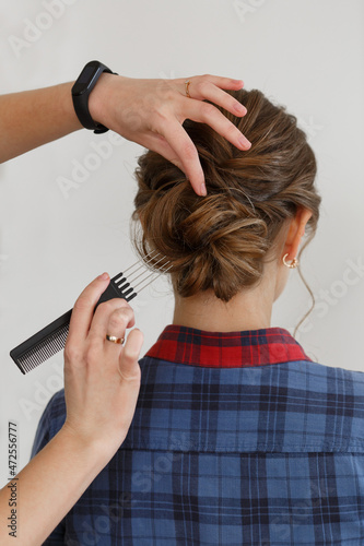 process hair styling in hairdressing salon. Professional haircutter makes beautiful wedding hairstyle hands of Hairstyle master with comb makes evening festive hairstyle for young woman on background 