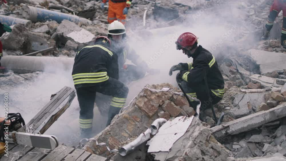 Men in protective uniforms and hardhats removing pieces of broken building during rescue mission after earthquake