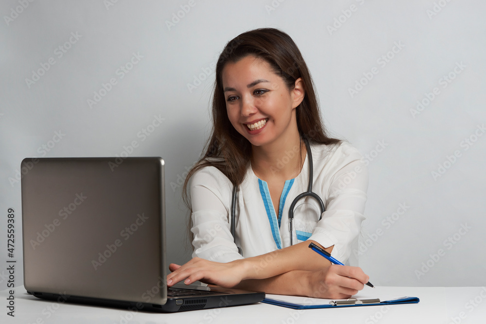 Young woman doctor sitting at office desk and working on laptop Young woman doctor sitting at office desk and working on laptop