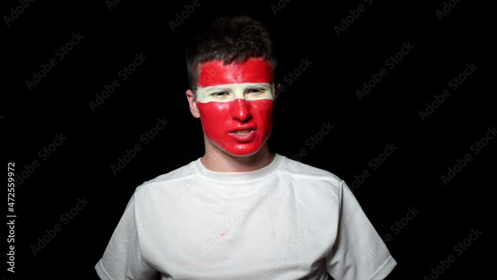 Happy fan celebrate victory of his team. Young man with face painted in national colours. Portrait of a happy man supports his national team at home Happy fan celebrate victory of his team. Young man with face painted in national colours. Portrait of a happy man supports his national team at home