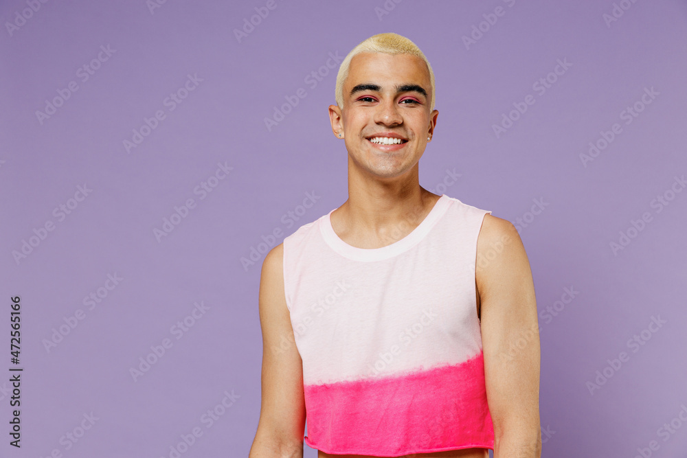 Young smiling fun blond hispanic latin gay man 20s with make up wearing bright pink top look camera isolated on plain pastel purple background studio portrait. People lifestyle fashion lgbtq concept. Young smiling fun blond hispanic latin gay man 20s with make up wearing bright pink top look camera isolated on plain pastel purple background studio portrait. People lifestyle fashion lgbtq concept.