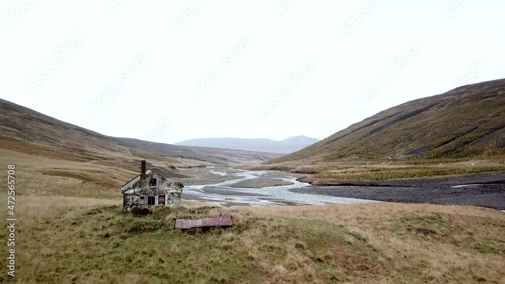 Dolly raising shot of a beautiful abandoned shack overlooking several gorgeous glacial streams and rolling mountain hills in a European nordic landscape.