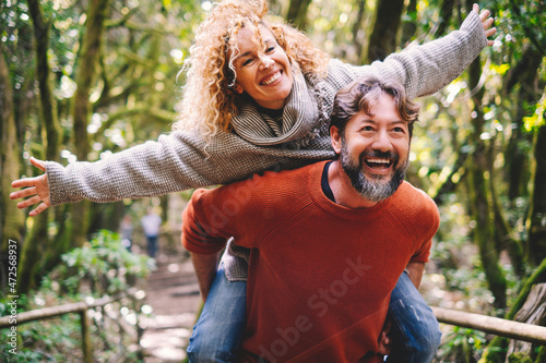 Overjoyed adult couple have fun together at outdoor park in leisure activity. Man carrying woman in piggyback and laugh a lot. Love and life mature people lifestyle concept. Enjoying vacation nature photo