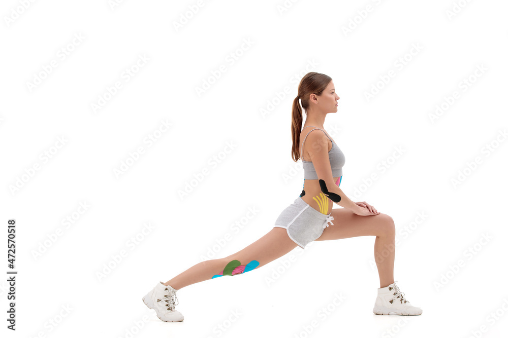 Kinesiology taping. Kinesiology tape on patient knee,hip, shoulder. Young female athlete doing exercises. Post traumatic rehabilitation,weight loss,cellulite removal, isolated on white background Kinesiology taping. Kinesiology tape on patient knee,hip, shoulder. Young female athlete doing exercises. Post traumatic rehabilitation,weight loss,cellulite removal, isolated on white background
