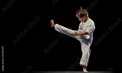 Photos Full-length portrait of little boy, karateka, training martial art isolated over black background