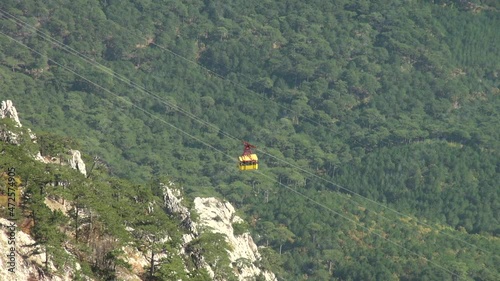View of yellow cabin descending from Mount Ai-Petri on cable car. Under cabin is forest of evergreen and deciduous plants. Calm and serene life on peninsula after annexation of Crimea to Russia.
