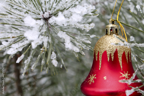 Red glass bell among pine branches covered with snow. Festive decoration. New Year. 