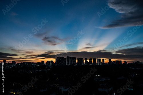 Canvas Print Colourful sunset with rays of sun and silhouette of city skyline and clouds