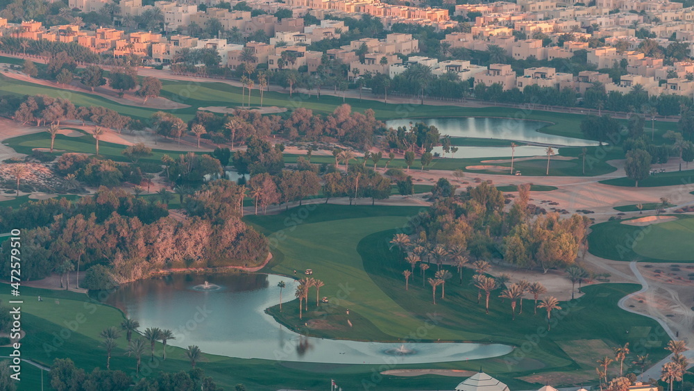 Aerial view to Golf course with green lawn and lakes, villas and houses behind it timelapse.