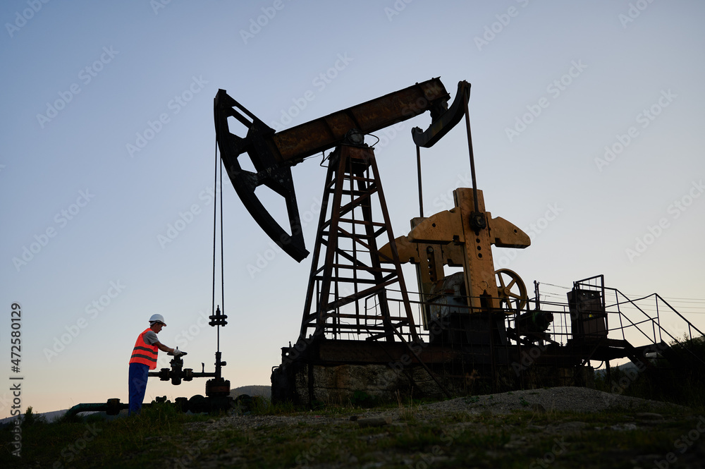 Capable professional inspector checking serviceability of pump jack during shift job at crude oil station, Caucasian man developing drilling rig and extract natural resources at refinery digger Capable professional inspector checking serviceability of pump jack during shift job at crude oil station, Caucasian man developing drilling rig and extract natural resources at refinery digger