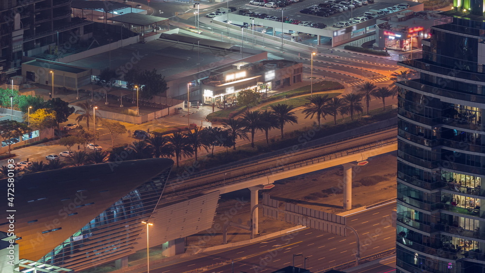 Futuristic buildings of Dubai with metro station and luxury skyscrapers behind near Dubai Marina night timelapse