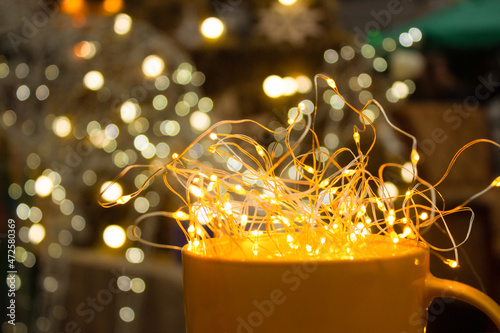 Close up view of yellow mug with illumination lights around. Christmas market with illuminating background, copy space