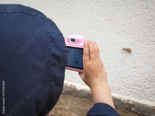 Cute kid taking picture on a snail after the rain with small pink camera