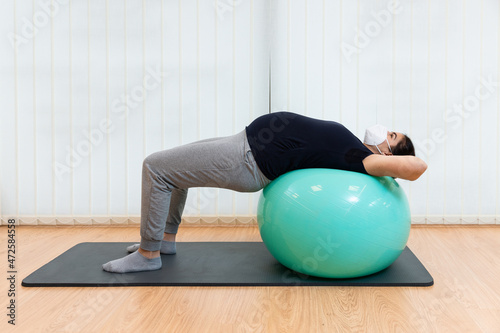 A pregnant woman laying on her back on a fitness ball doing exercises