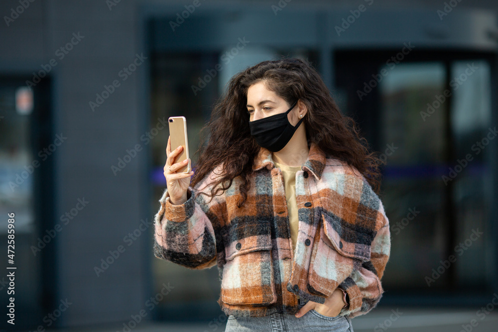 Fototapeta premium Portrait of young woman wearing safety mask. Beautiful girl with face mask using mobile phone.