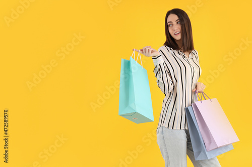 Attractive woman with shop bags on yellow background