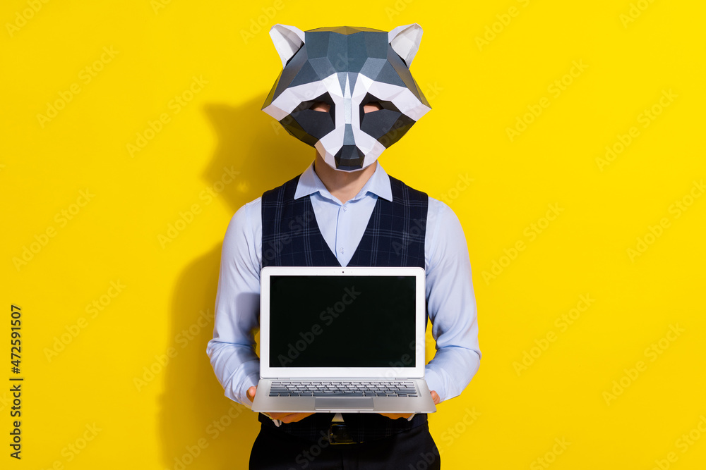 Photo of confident guy demonstrate pc screen empty space wear raccoon mask vest isolated yellow color background