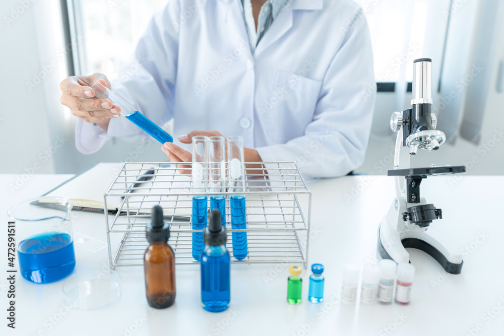 Scientist woman holding test tube in his hands and checking blue liquid from test tube while working Scientist woman holding test tube in his hands and checking blue liquid from test tube while working
