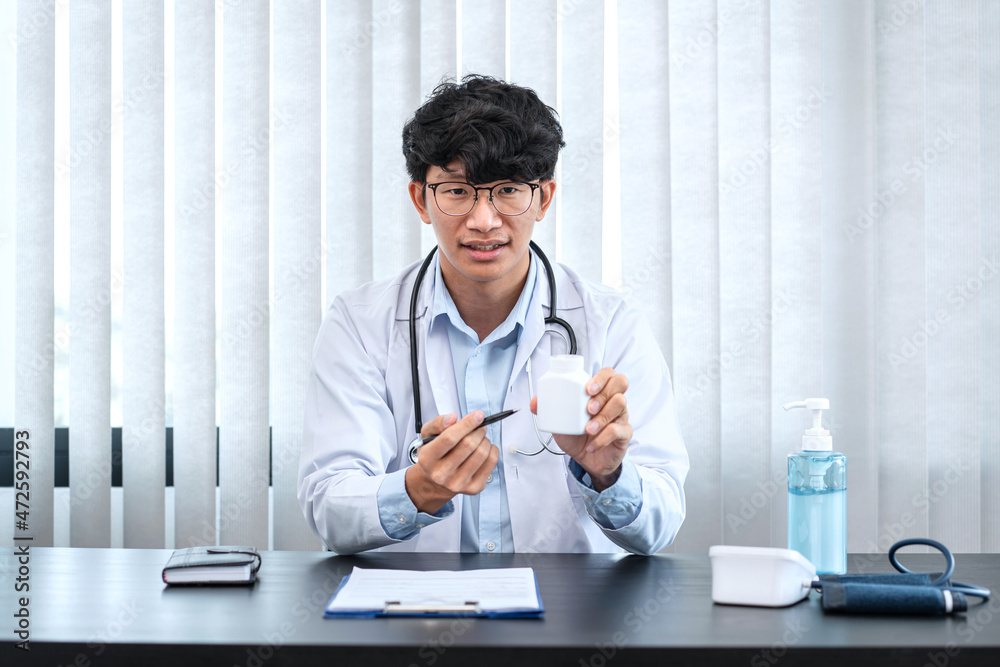 Male doctor showing and pointing bottle of pills in hands after diagnose disease the patient and writing prescribing