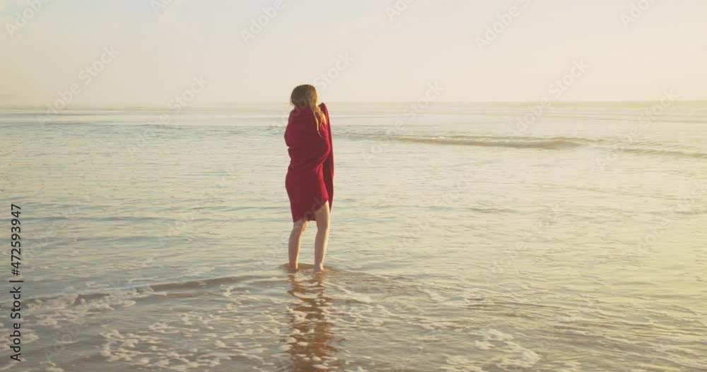 A young lady standing in the ocean waves enjoying a golden, chilly sunset . A young lady standing in the ocean waves enjoying a golden, chilly sunset .