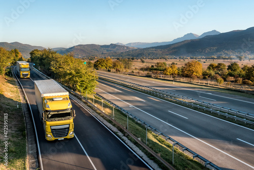 Two yellow Transportation trucks on the road near entrance to a highway or motorway. Business Transportation and Trucking Industry.