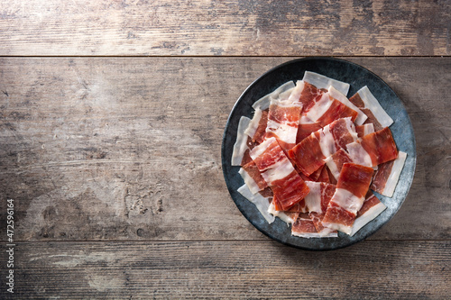 Spanish serrano ham slices on black plate on wooden table. Copy space photo