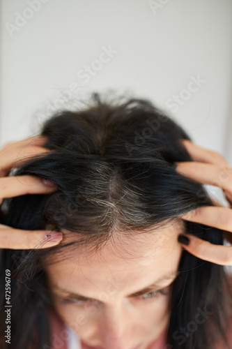 Portrait of a beautiful young woman examining her scalp and hair in front of the mirror,