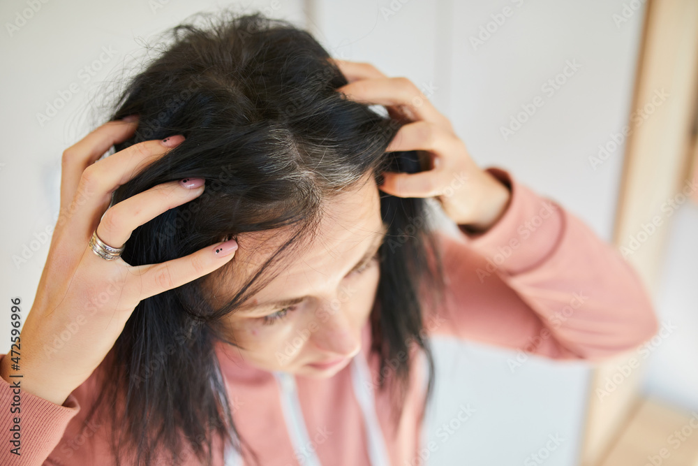 Fototapeta premium Portrait of a beautiful young woman examining her scalp and hair in front of the mirror,