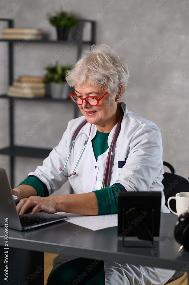elderly woman doctor works at the computer. Telemedicine doctor talking to patient using laptop elderly woman doctor works at the computer. Telemedicine doctor talking to patient using laptop