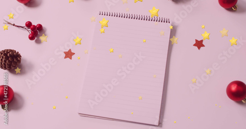 Image of gold stars falling over christmas decorations and notepad with copy space