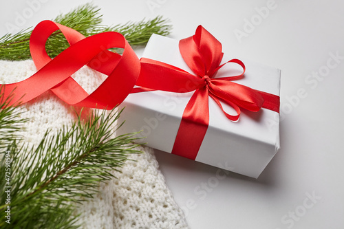 Christmas gift box with red ribbon and knitted sweater with green pine tree branches on white © mikeosphoto