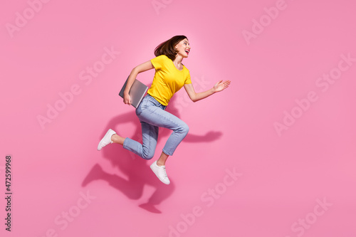 Photo of cute pretty young lady dressed yellow clothes smiling hurrying jumping carrying modern gadget isolated pink color background