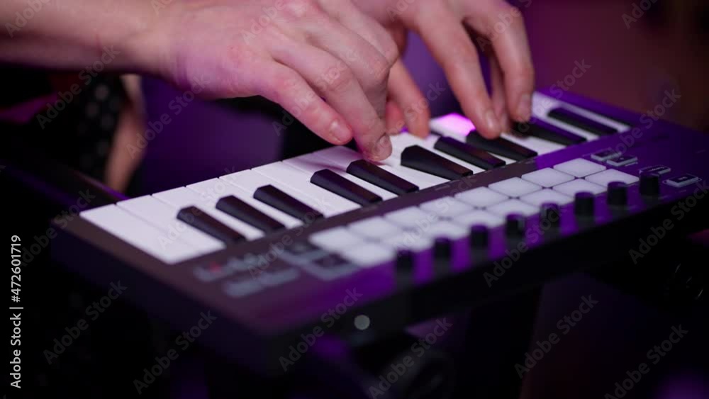 Close-up of the hands of a DJ girl without a manicure, who performs a melody on a synthesizer, adjusts the settings of the instrument in the club with purple lighting Close-up of the hands of a DJ girl without a manicure, who performs a melody on a synthesizer, adjusts the settings of the instrument in the club with purple lighting