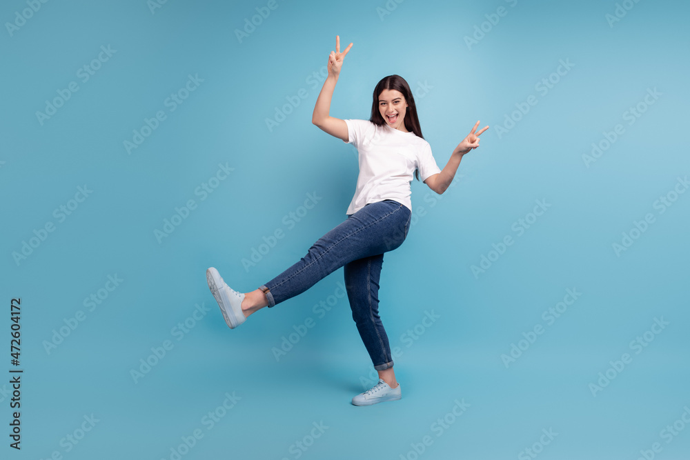 Full body profile side photo of young excited girl show fingers peace v-symbol isolated over blue color background Full body profile side photo of young excited girl show fingers peace v-symbol isolated over blue color background