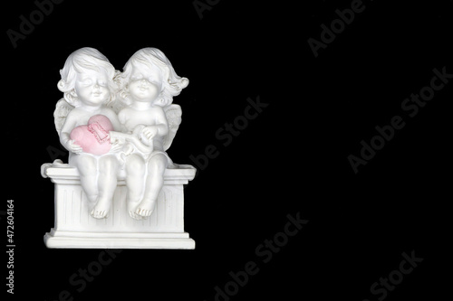 Two angels are sitting on a bench and holding a heart with a key in their hands