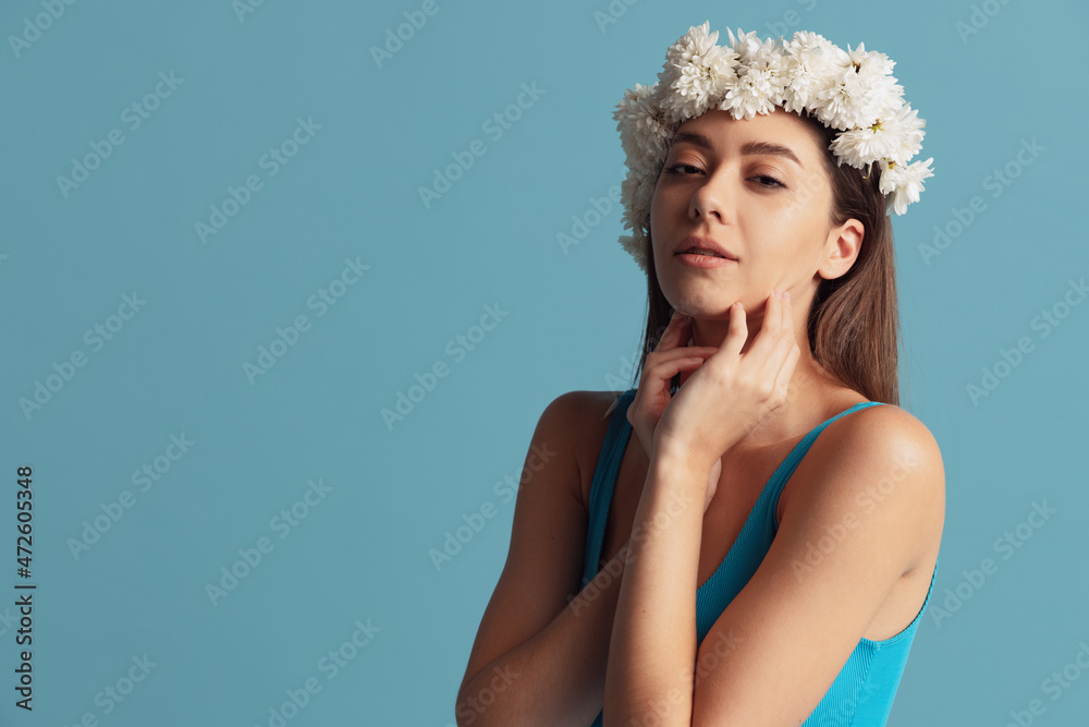 Pretty charming girl in wreath of flowers posing isolated over blue color studio background. Natural beauty concept. Pretty charming girl in wreath of flowers posing isolated over blue color studio background. Natural beauty concept.