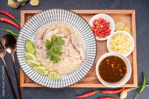 Steamed rice topped with chicken on wooden background, Hainanese chicken rice served with chili sauce on a wooden background.
