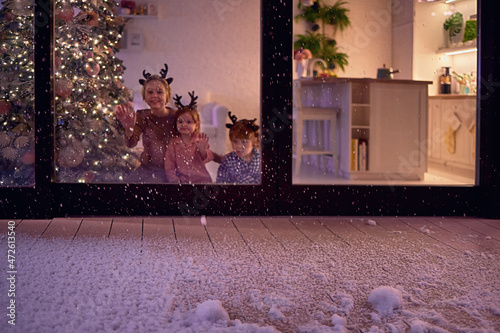 snow flakes falling on the patio at magical chrismas night, with happy kids watching it at the background