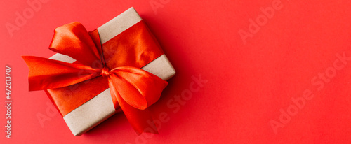 Banner made of Present box with red bow on red background. Flat lay, top view, copy space.
