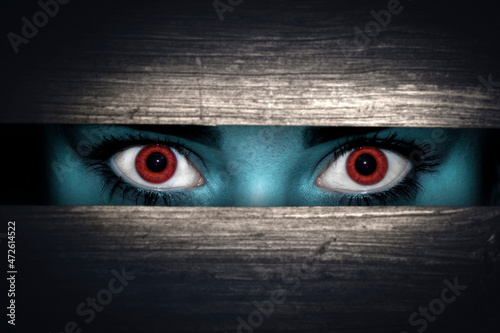 Scary, not human look through a crack in the dark with red eyes photo