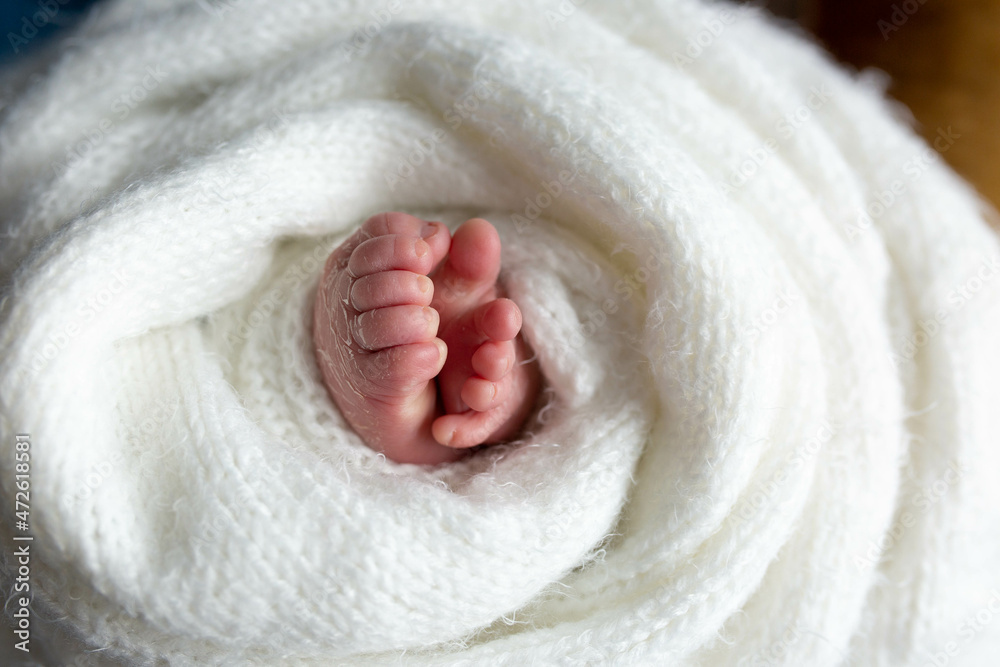 a small leg of the newborn in a white scarf. soft focus a small leg of the newborn in a white scarf. soft focus