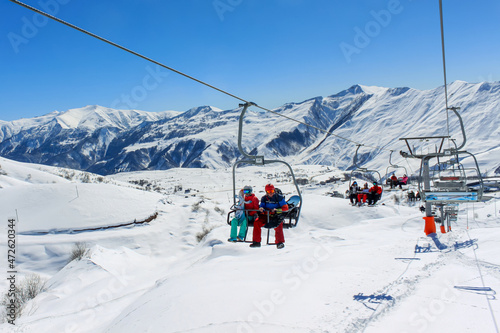 People on a chairlift ascend a ski slope. In the background snowy mountain ridge and clear blue sky. Active winter holidays in the mountains. photo