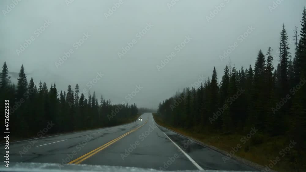Passenger front view through windscreen of car driving on Highway 93 in Kootenay National Park, British Columbia, Canada on rainy day in autmn with wet road, forests and operating wiper. Passenger front view through windscreen of car driving on Highway 93 in Kootenay National Park, British Columbia, Canada on rainy day in autmn with wet road, forests and operating wiper.