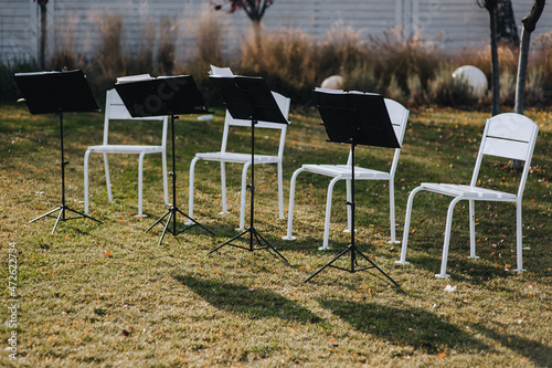 Four chairs and stands with musical notes stand on the green grass in the park, garden. Waiting for the concert.