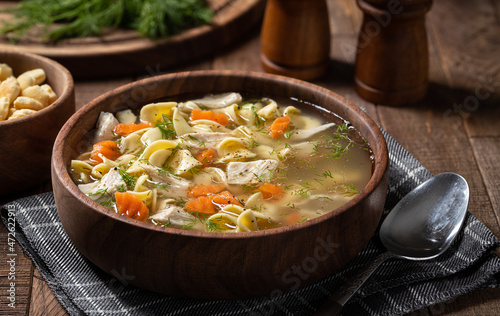 Bowl of chicken noodle soup on a wooden table photo