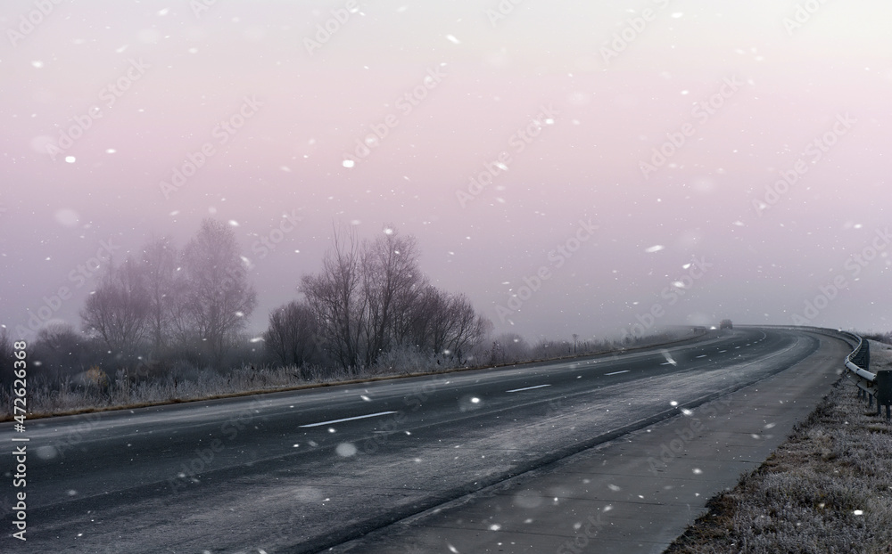 A sharp turn in the road in an early frosty morning and falling snow.