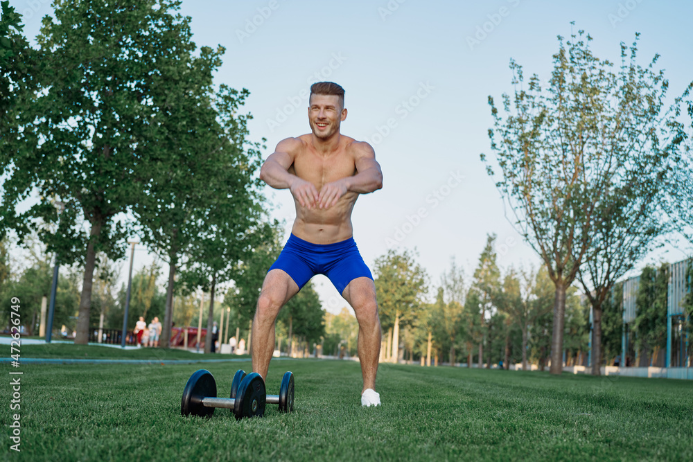 Muscled man in the park training with dumbbells